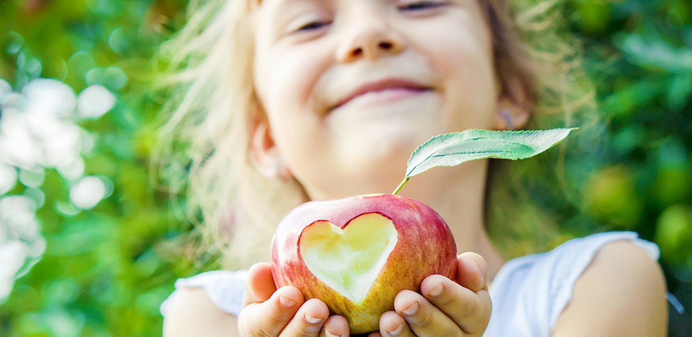 Mädchen lächelt und hält Apfel mit Herz in die Kamera